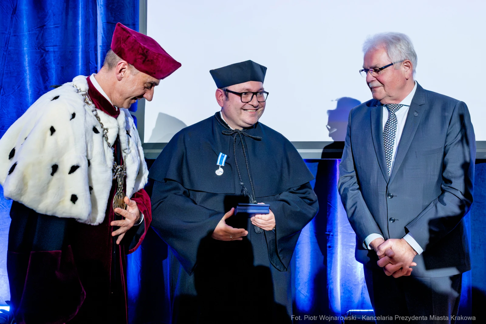 Trzech mężczyzn w akademickich togach podczas ceremonii wręczenia nagrody.  Autor: Piotr Wojnarowski