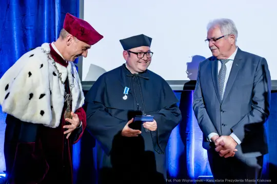 Trzech mężczyzn w akademickich togach podczas ceremonii wręczenia nagrody.
