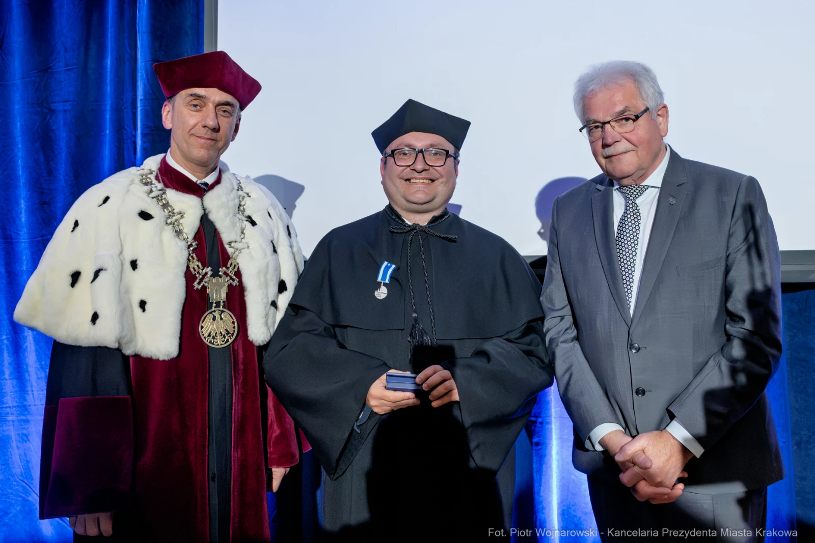 Trzej mężczyźni w akademickich togach, jeden z medalem, podczas ceremonii wręczenia nagród.  Autor: Piotr Wojnarowski
