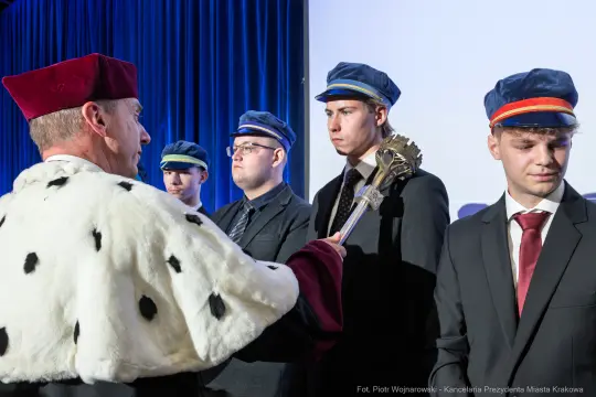 Ceremonia z udziałem mężczyzn w garniturach i czapkach, jeden z nich w królewskim płaszczu.