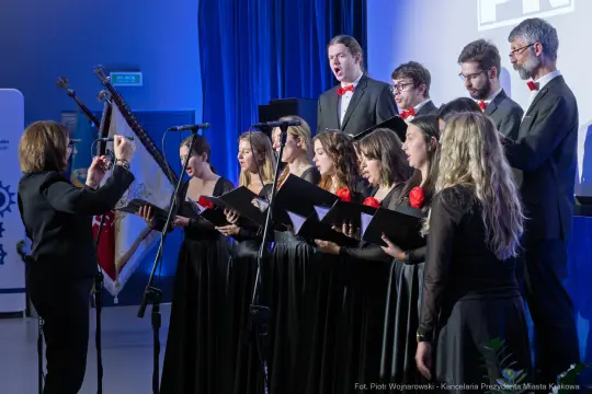 Chór w eleganckich strojach wykonujący utwór muzyczny.