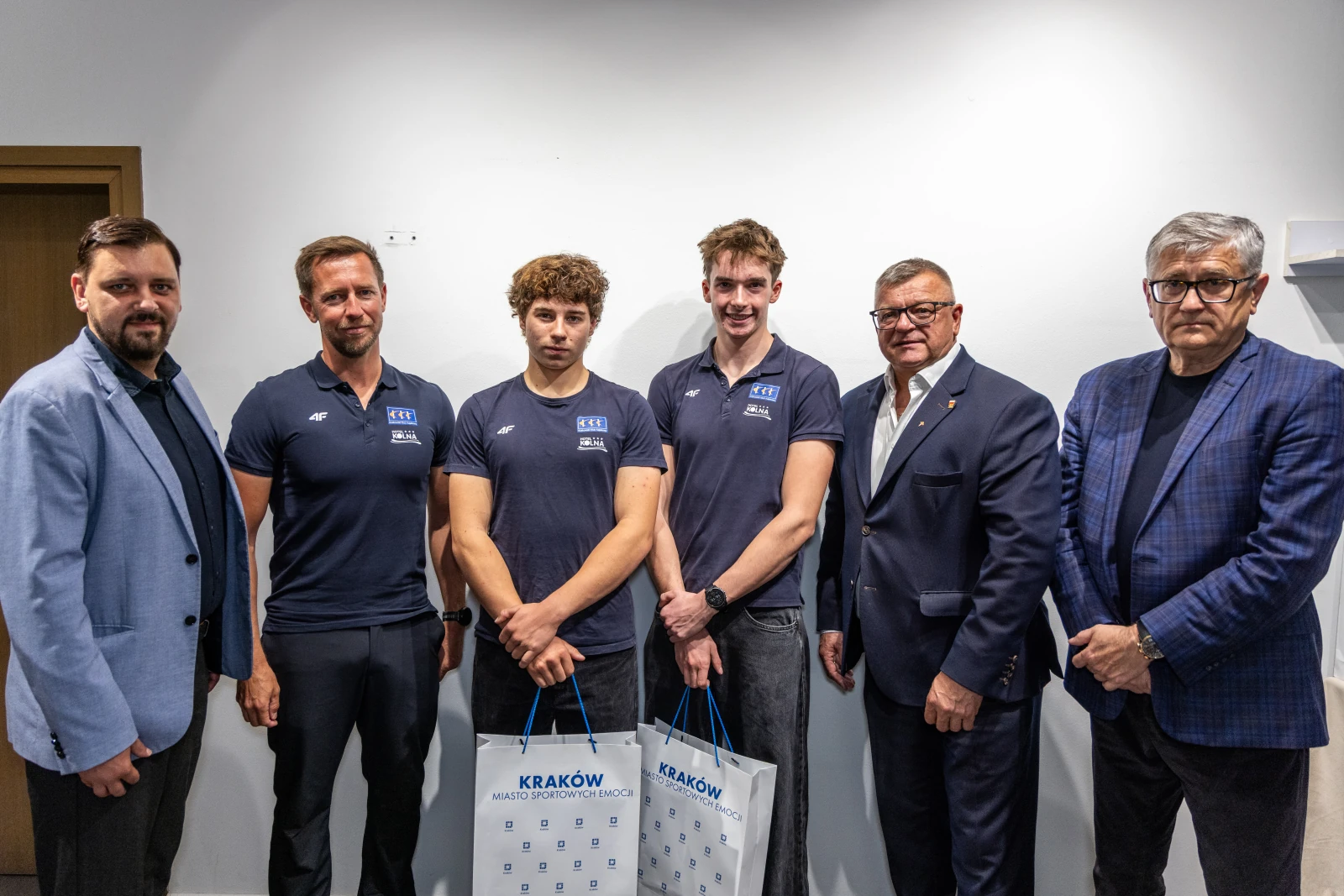 Grupa mężczyzn w strojach sportowych z torbami, stojąca w pomieszczeniu.  Autor: Jan Graczyński