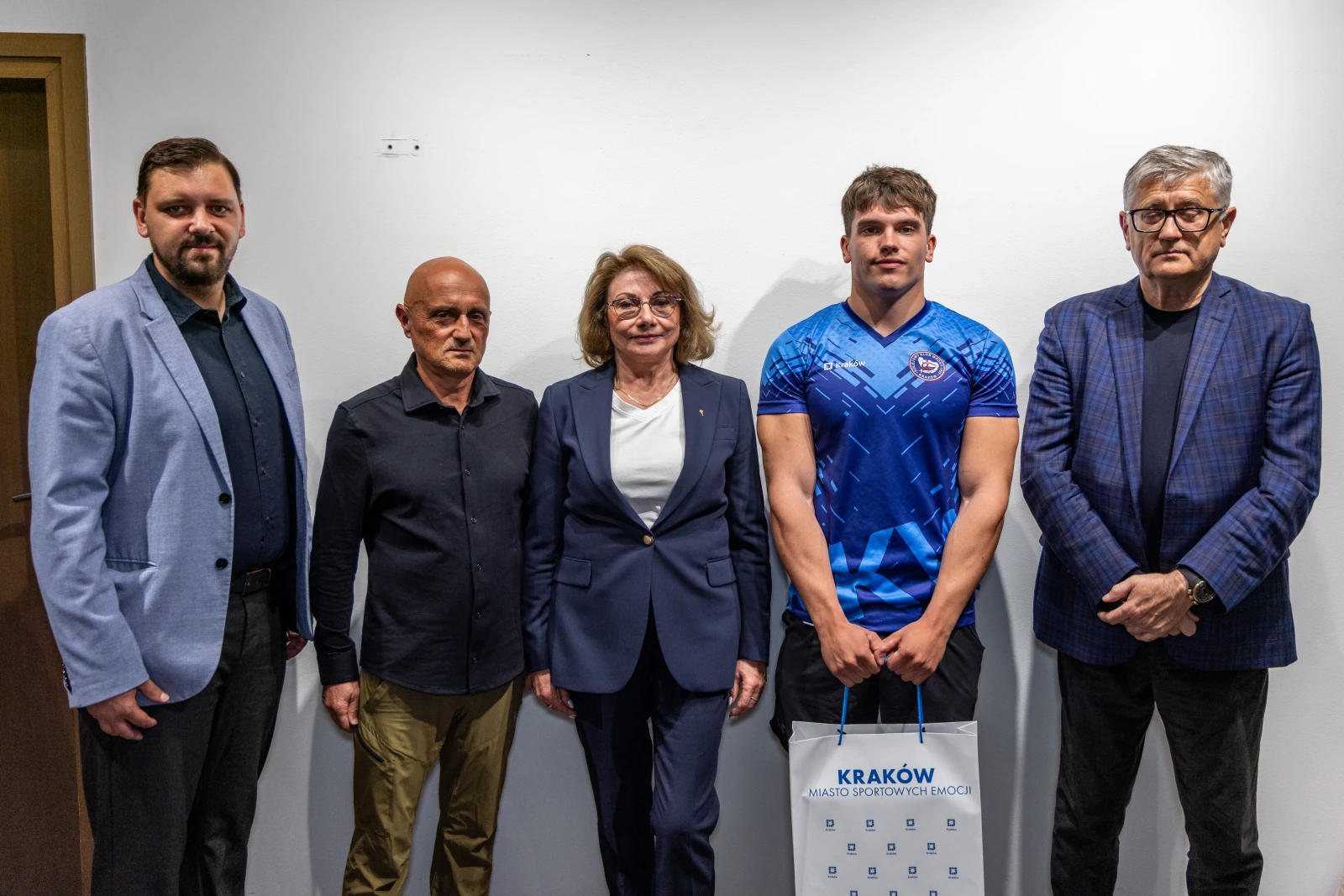 Grupa pięciu osób w formalnych strojach, jedna z nich trzyma torbę z logo Krakowa.  Autor: Jan Graczyński