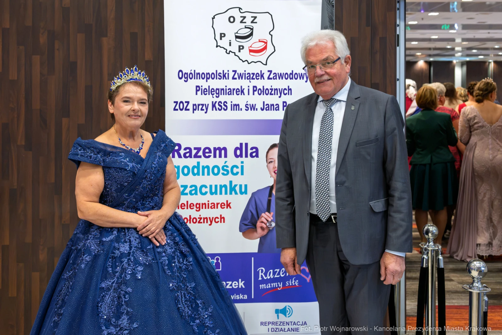 Kobieta w niebieskiej sukni z koroną i mężczyzna w garniturze na tle banera z napisem o pielęgniarkach.  Autor: Piotr Wojnarowski
