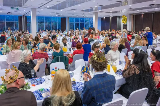 Uczestnicy wydarzenia siedzą przy stołach, rozmawiają i bawią się w eleganckiej sali.