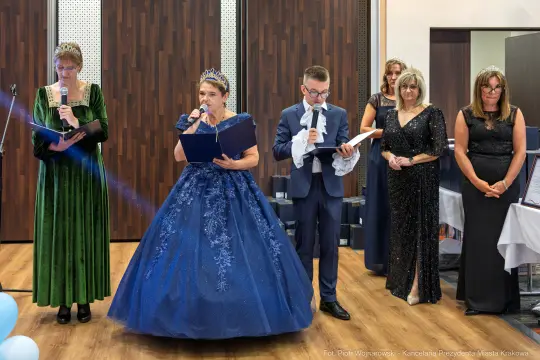 Uroczystość z wystąpieniami, eleganckie stroje, goście w formalnych kreacjach.
