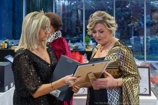 Dwie kobiety w eleganckich strojach rozmawiają i przeglądają dokumenty.