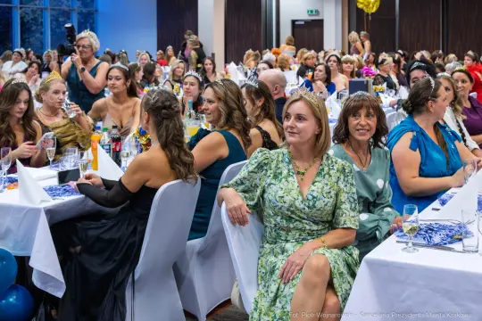 Tłum ludzi na eleganckim przyjęciu, kobiety w sukienkach, stoły z napojami i dekoracjami.