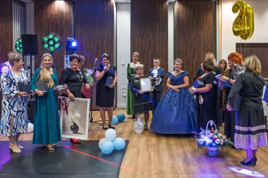 Grupa kobiet w eleganckich strojach, z koronami, podczas uroczystości wręczenia nagród.