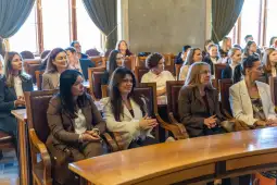 Grupa kobiet siedzących w sali, uczestniczących w wydarzeniu lub spotkaniu.