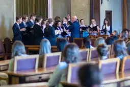 Chór wykonujący utwór muzyczny w sali z widownią.