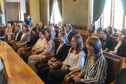 Grupa kobiet siedzących w sali, uczestniczących w wydarzeniu lub spotkaniu.