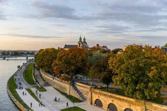 Widok na rzekę z drzewami w jesiennych kolorach oraz budynkiem z wieżami w tle.