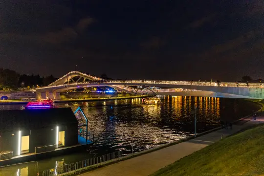 Most oświetlony nocą, odbijający się w wodzie, z łodzią na rzece.