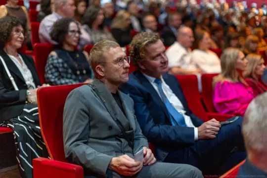 Mężczyźni siedzący na widowni w teatrze, w tle publiczność.