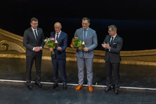 Czterech mężczyzn na scenie z kwiatami i nagrodami.