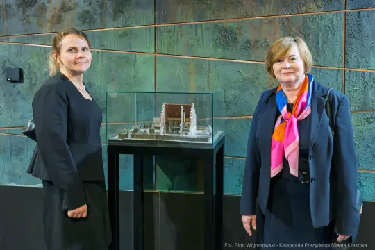 Dwie kobiety stoją obok modelu budynku w szklanej gablocie.
