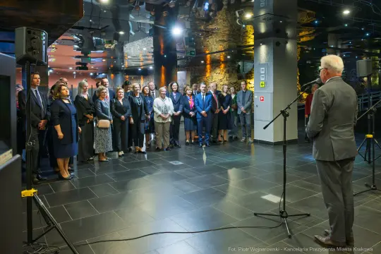 Grupa ludzi w eleganckich strojach podczas wydarzenia w nowoczesnym wnętrzu.