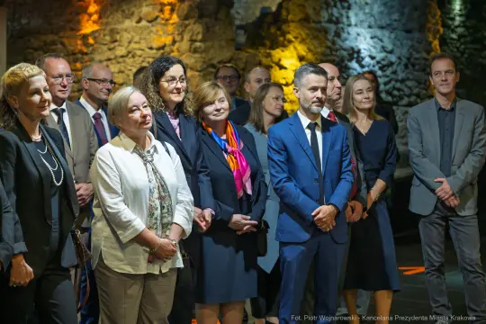 Grupa ludzi w eleganckich strojach na wydarzeniu w historycznym wnętrzu.
