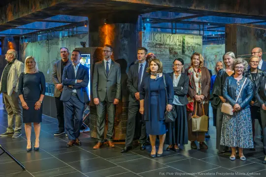 Grupa ludzi w eleganckich strojach na wydarzeniu kulturalnym w nowoczesnym wnętrzu.