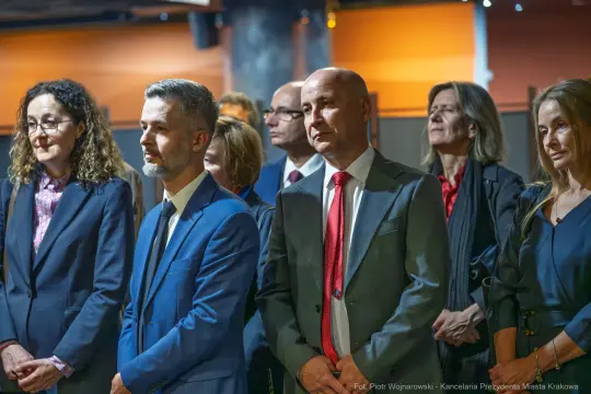 Grupa ludzi w formalnych strojach, skupionych na wydarzeniu.
