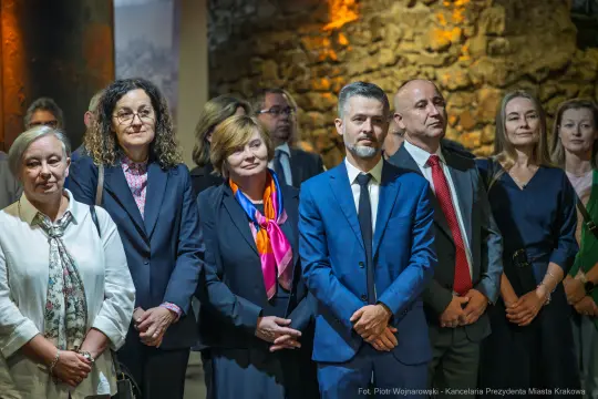 Grupa osób w formalnych strojach podczas wydarzenia w historycznym wnętrzu.