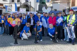 Grupa ludzi w niebieskich koszulkach z transparentami i plakatami podczas wydarzenia na świeżym powietrzu.