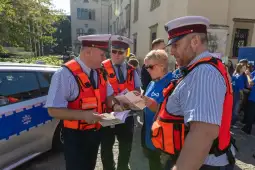 Funkcjonariusze w kamizelkach odblaskowych rozmawiają z kobietą, trzymając ulotki.