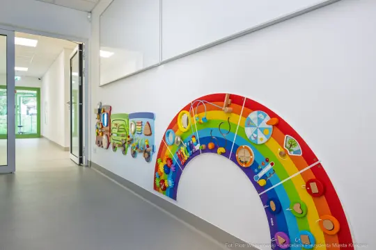Tęczowa ściana z interaktywnymi elementami edukacyjnymi dla dzieci.