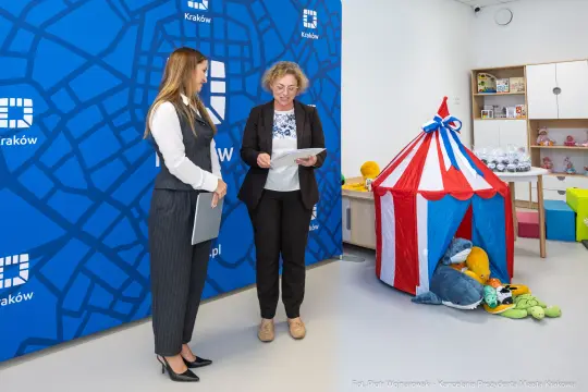 Dwie kobiety rozmawiają w kolorowym pomieszczeniu z namiotem dla dzieci i zabawkami.