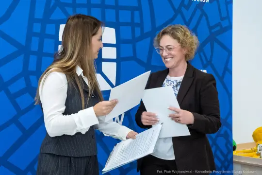 Dwie kobiety wymieniają się dokumentami w biurze.