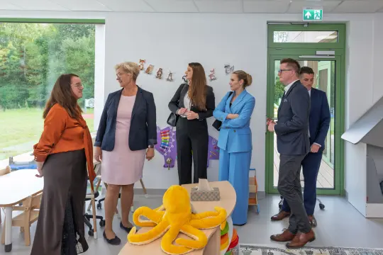 Grupa osób w kolorowych strojach w nowoczesnej sali przedszkolnej z zabawkami.