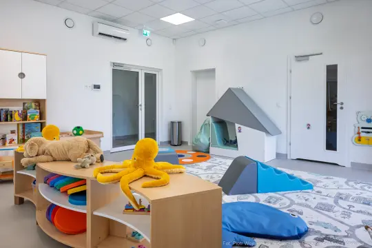 Pokój zabaw dla dzieci z kolorowymi dywanami, zabawkami i miękkimi elementami do zabawy.
