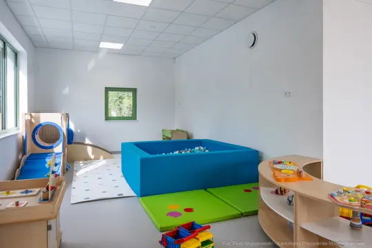 Pokój zabaw dla dzieci z niebieskim basenem z piłkami i kolorowymi matami.