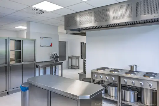 Nowoczesna kuchnia z metalowymi meblami, piecami i sprzętem gastronomicznym.