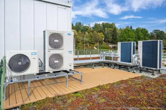 Instalacja systemu klimatyzacji z jednostkami zewnętrznymi i rurami na tle zieleni.
