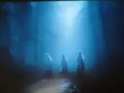 Trzy postacie w białych szatach w mglistej, niebieskiej scenerii leśnej.