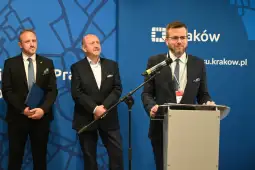 Konferencja prasowa w Krakowie z udziałem trzech mężczyzn, jeden z nich przemawia.