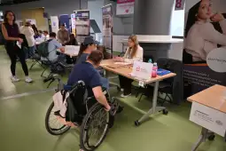 Osoba na wózku inwalidzkim rozmawia z przedstawicielem firmy podczas targów pracy.