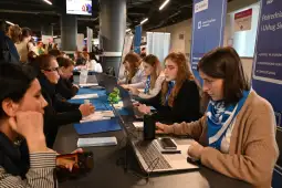 Tłum ludzi przy stoiskach informacyjnych, pracownicy obsługujący klientów.