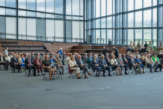 Grupa ludzi siedzących na krzesłach w dużej sali.