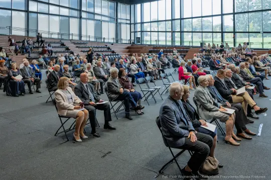 Zgromadzenie osób siedzących na krzesłach w sali konferencyjnej.