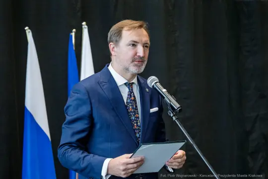 Mężczyzna w garniturze przemawia do mikrofonu, trzymając dokument.