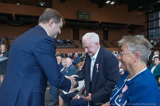 Uroczystość wręczenia odznaczeń, mężczyzna podaje rękę starszemu mężczyźnie.
