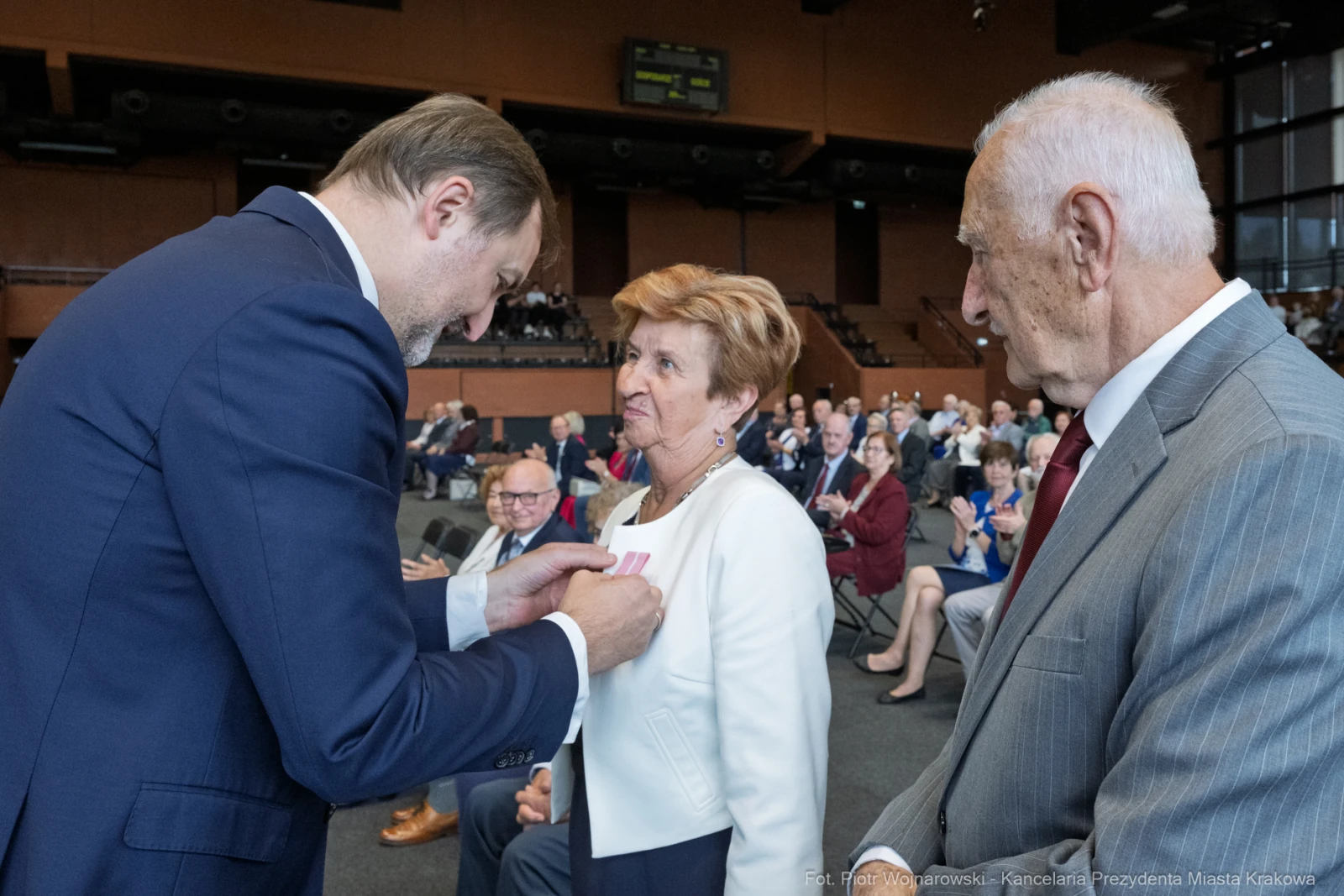 Wręczenie odznaczenia kobiecie przez mężczyznę w obecności innych gości na uroczystości.  Autor: Piotr Wojnarowski