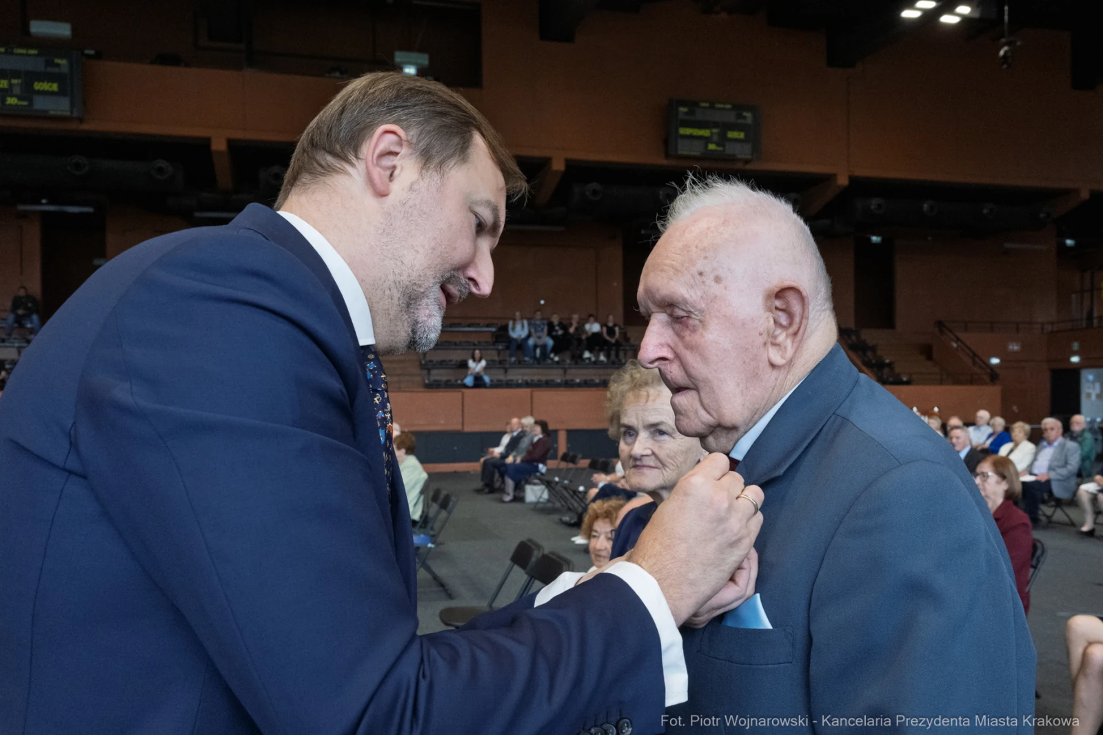 Uroczystość wręczenia odznaczenia starszemu mężczyźnie przez młodszego mężczyznę.  Autor: Piotr Wojnarowski