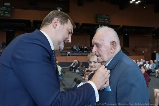 Uroczystość wręczenia odznaczenia starszemu mężczyźnie przez młodszego mężczyznę.