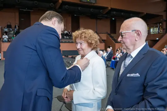 Uroczystość wręczenia odznaczeń, uśmiechnięta kobieta w białym garniturze.