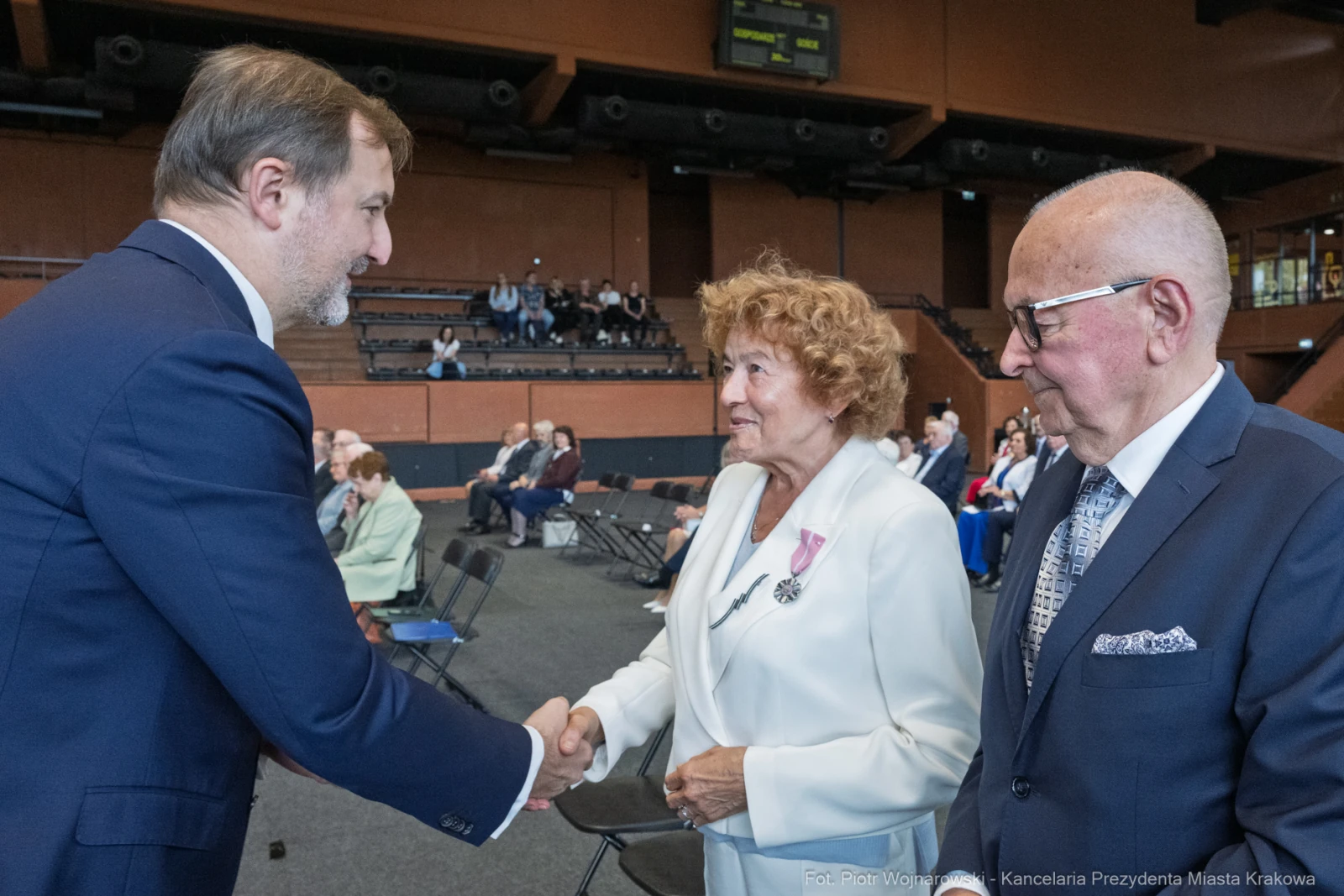 Uścisk dłoni między mężczyzną a kobietą w otoczeniu siedzących gości.  Autor: Piotr Wojnarowski