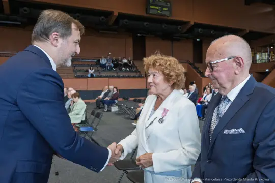 Uścisk dłoni między mężczyzną a kobietą w otoczeniu siedzących gości.